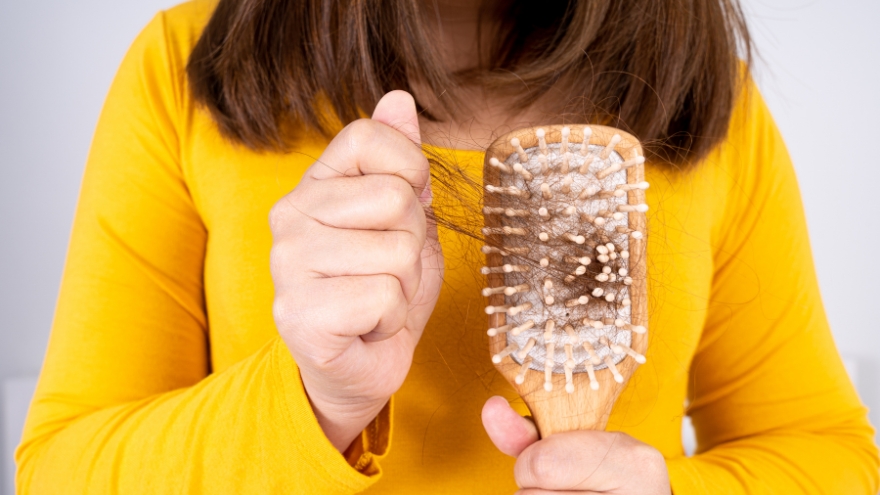 A woman in a yellow shirt pulls out hair from a hairbrush.