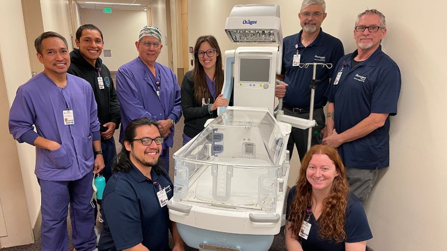 Clinical Engineers posing for a group photo in front of a new piece of pediatric medical technology.