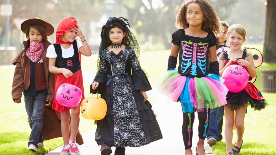 A group of young children in Halloween costumes trick-or-treating in their neighborhood.