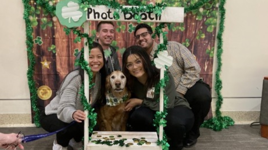 Members of the Patient Experience team pose with a therapy dog in a St. Patrick's Day-themed photo booth.