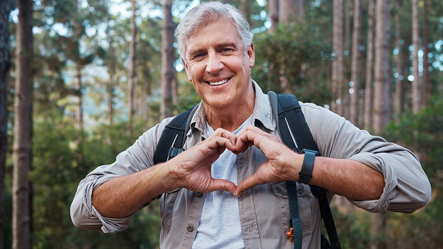 Mature man forming a heart shape with his hands while out hiking