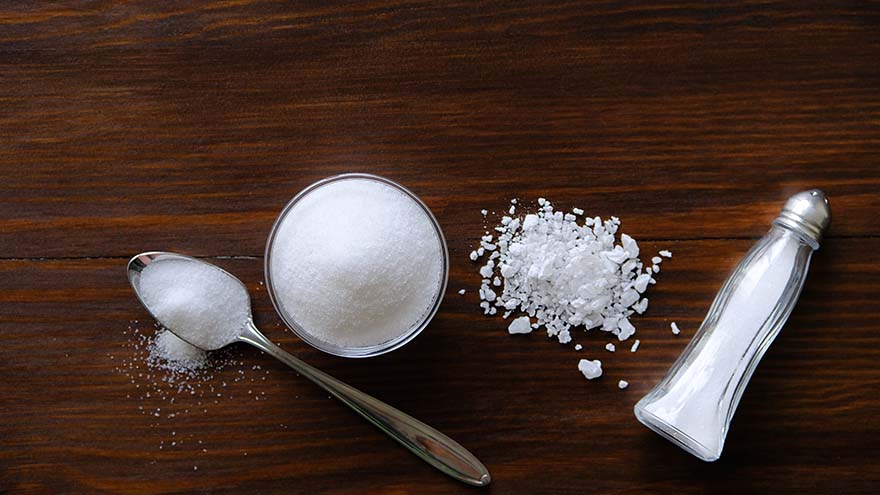 Natural, organic, sea, white salt in a spoon, in a Cup, in a salt shaker, poured on a wooden table.