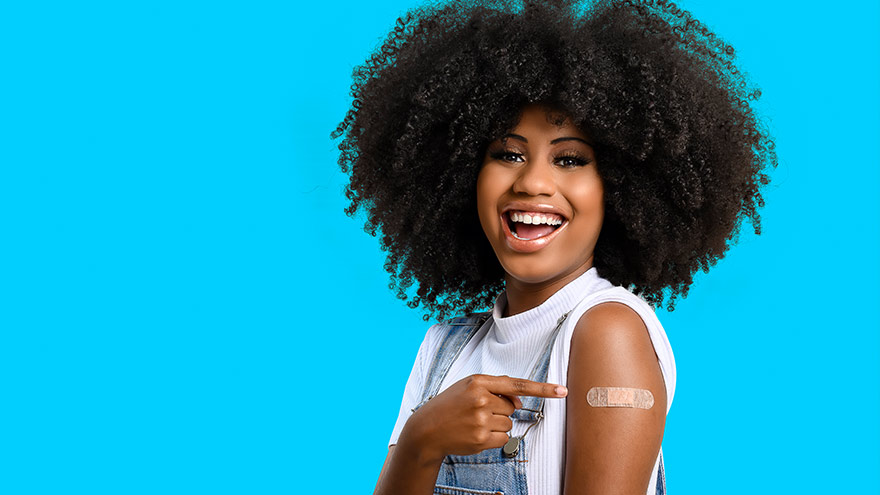 niño de cabello rubio sonriendo a la cámara mostrando una curita en la parte superior del brazo después de recibir la vacuna