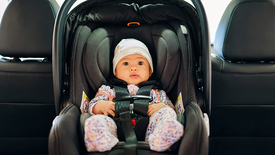 A 3 month old baby sitting in a carseat in the backseat of an auto