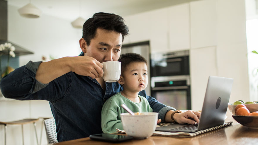 Father and son having breakfast together, using laptop